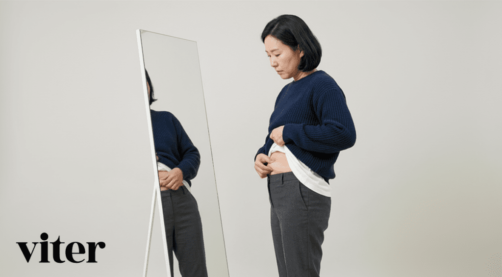 거울을 보며 셔츠 아래로 드러난 뱃살을 살피는 40대 중년 여성