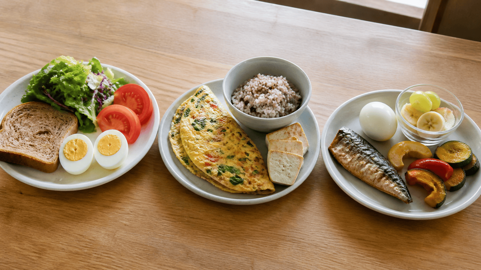 삶은 달걀, 빵, 샐러드, 오믈렛, 잡곡밥, 두부, 구운 생선, 채소, 과일로 구성된 세 접시 식사.