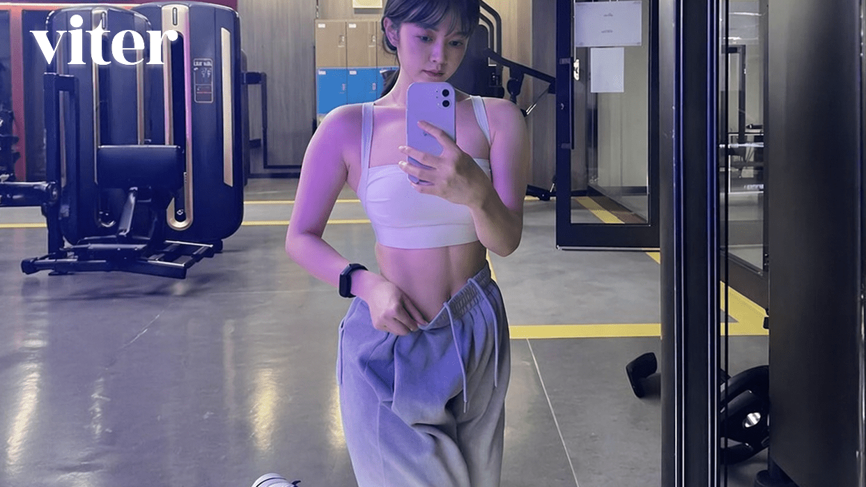젊은 여성이 헬스장 거울 앞에서 탄탄한 복근을 드러낸 채 셀카를 찍는다.